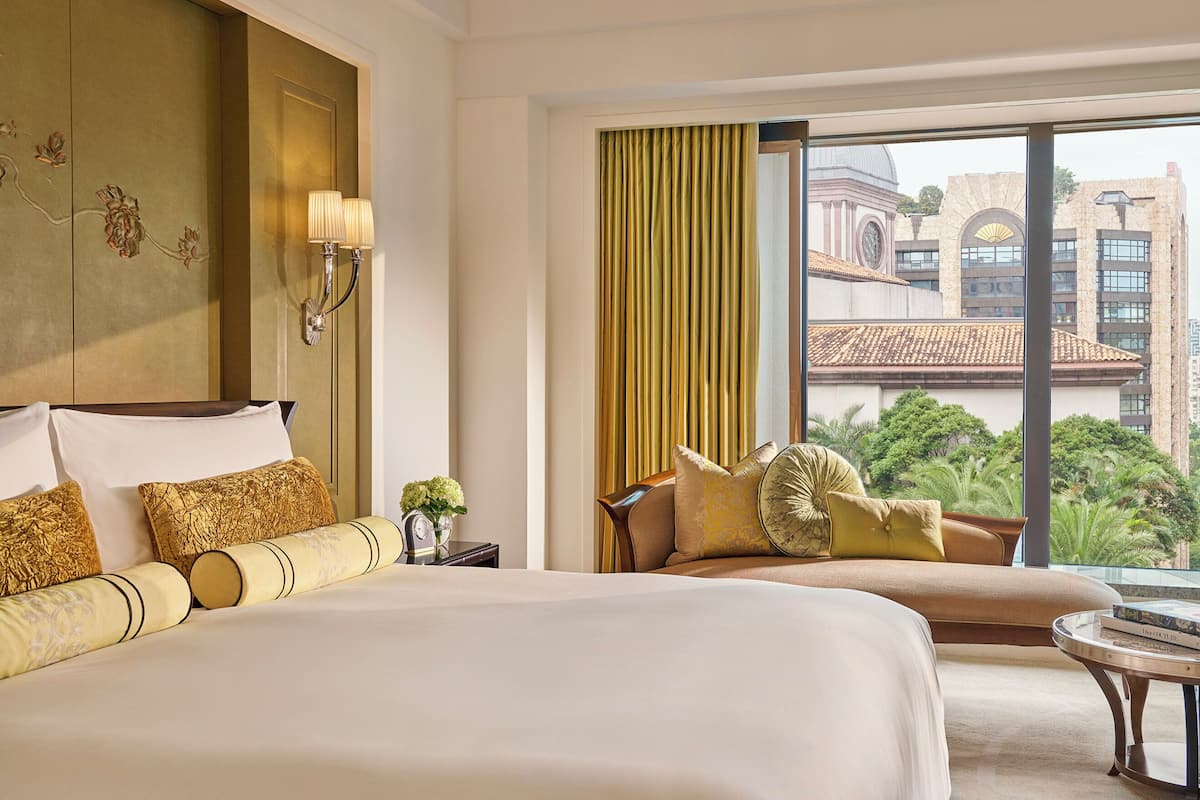 Ein Hotelzimmer mit einem großen Bett, einem Schlafsofa, einem runden Couchtisch und Blick auf eine Stadt durch große Fenster.