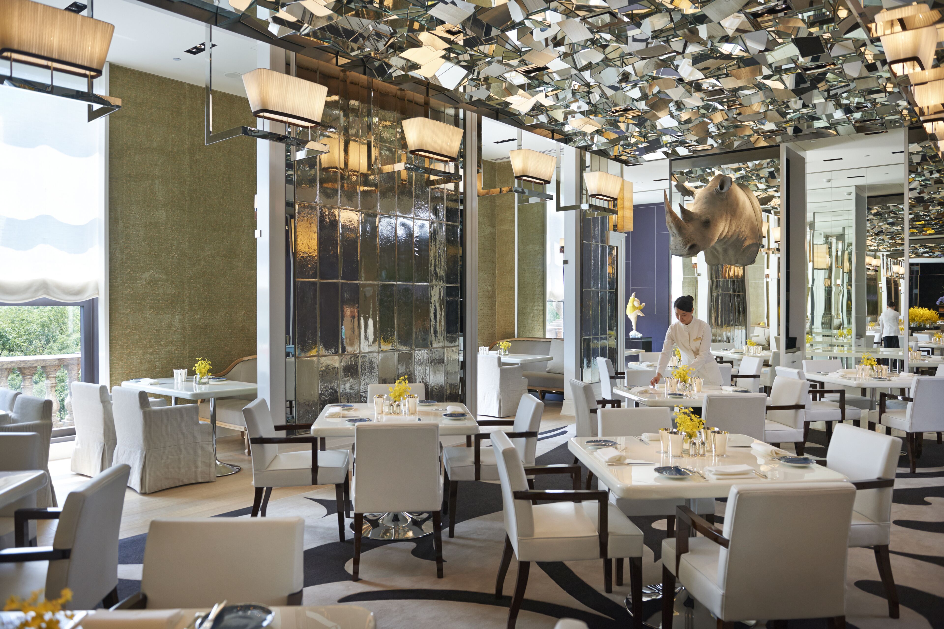Un restaurante moderno con techos altos, superficies reflectantes y un camarero atendiendo a los comensales.