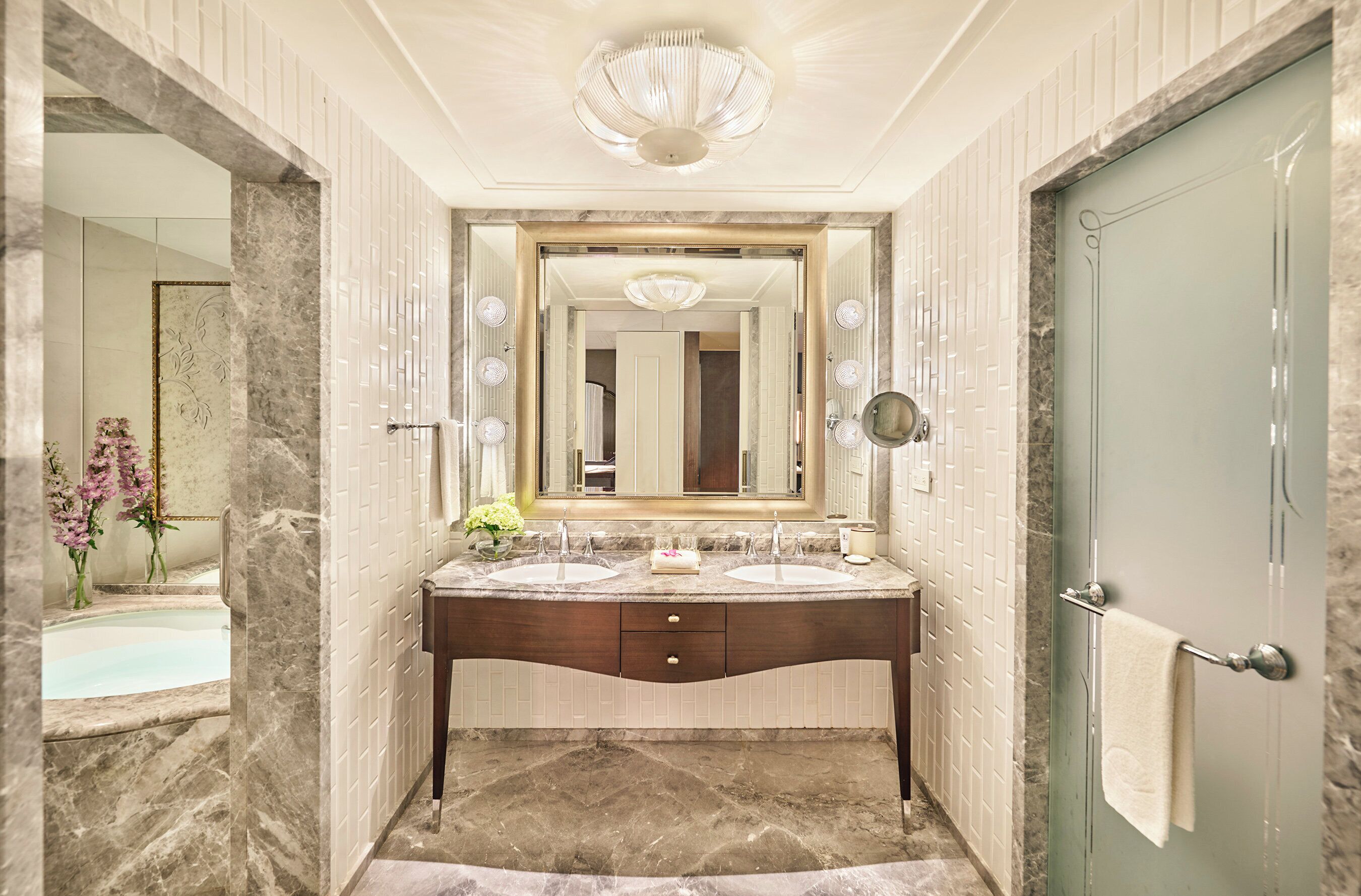 A bathroom with a marble vanity, two sinks, a large mirror, and a door with a towel rack.