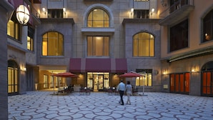 A hotel courtyard with a patterned floor, outdoor seating, and a central entrance with a red awning. - Mandarin Oriental, Taipei (Taipei)