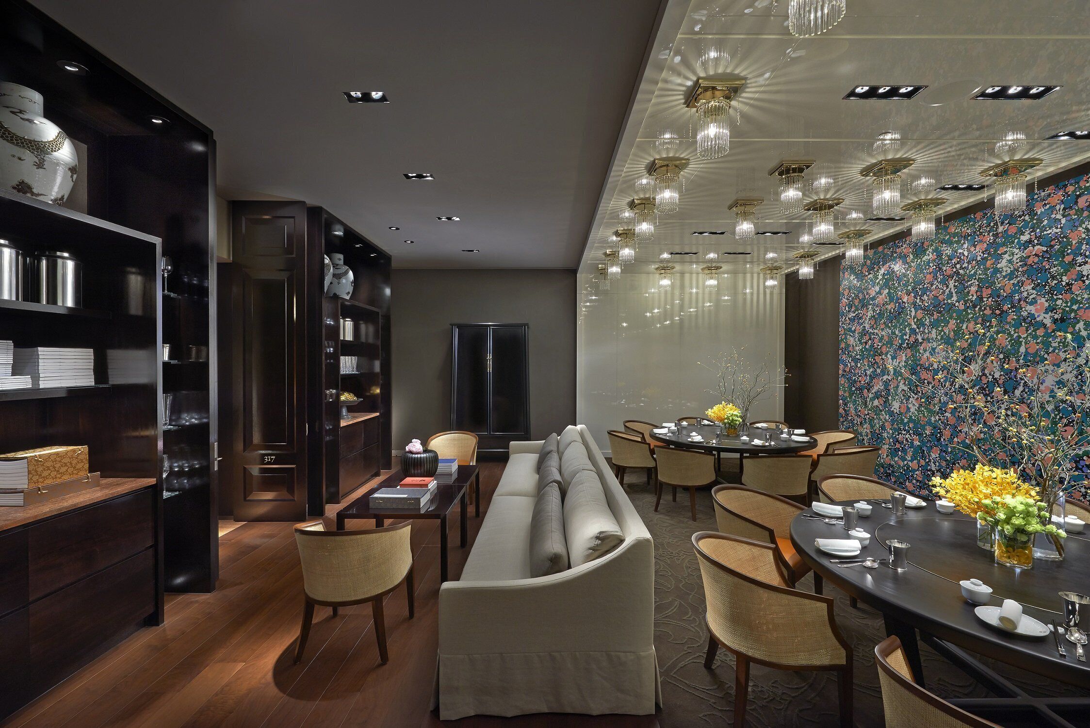 A modern dining area with a round table, chairs, and a floral wall.