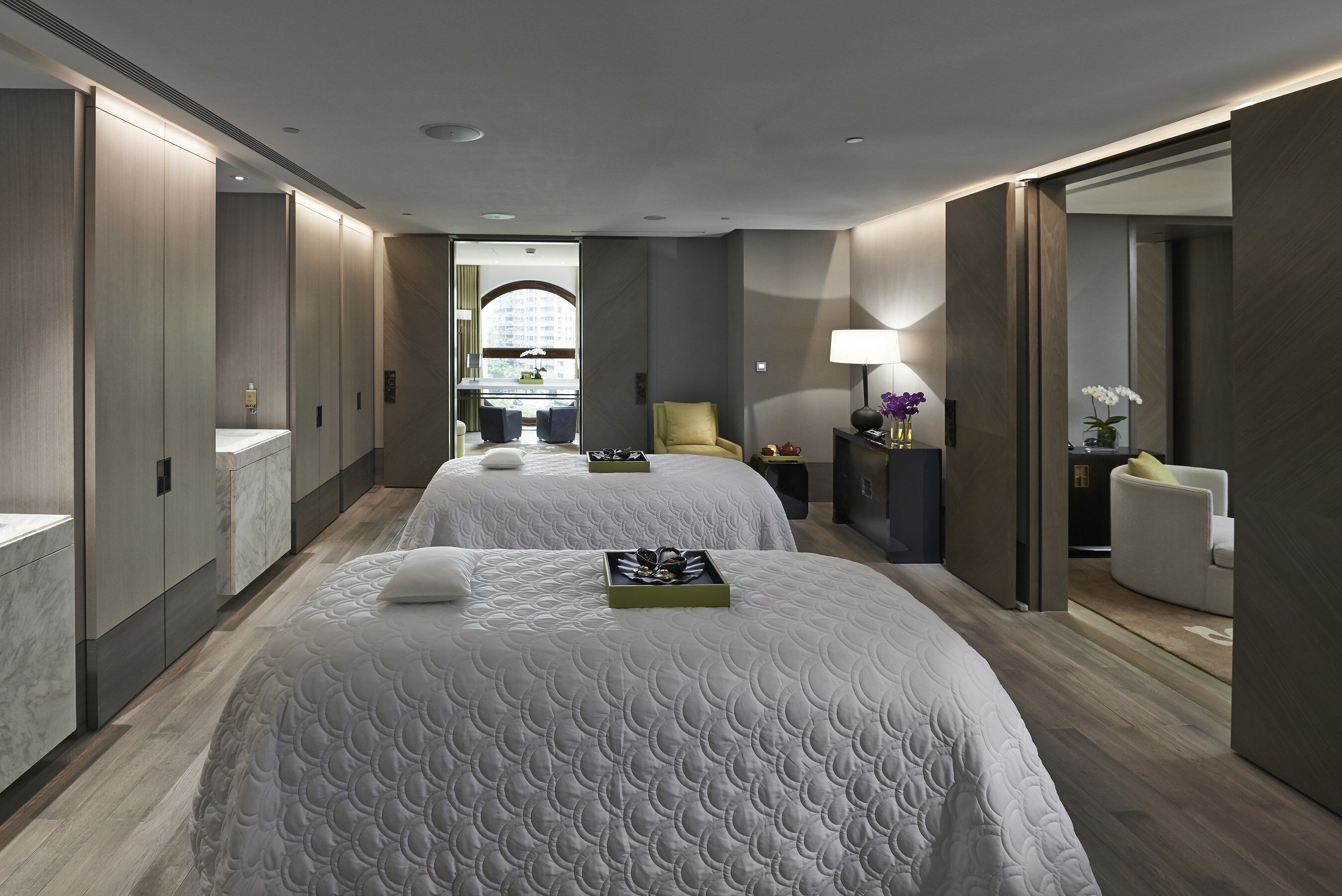 A hotel room with two beds, a sitting area with a chair, a desk, and a large mirror.