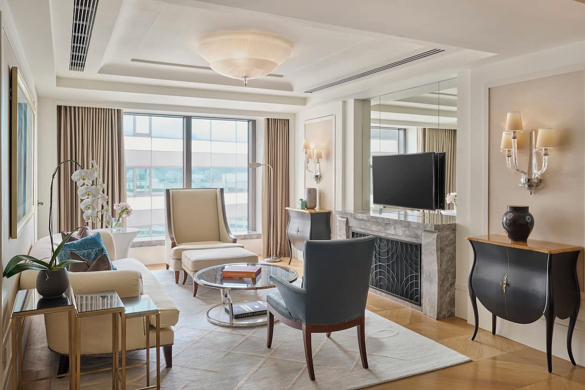 Ein modernes Hotelzimmer mit einer Couch, Sesseln, einem Couchtisch, einem Fernseher und einem Kamin.