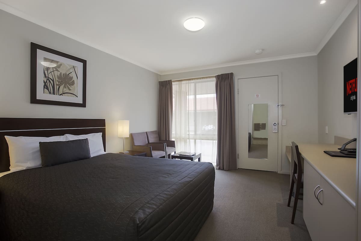 Habitación de hotel con una cama grande, un escritorio, una silla, un televisor y una ventana con cortinas.