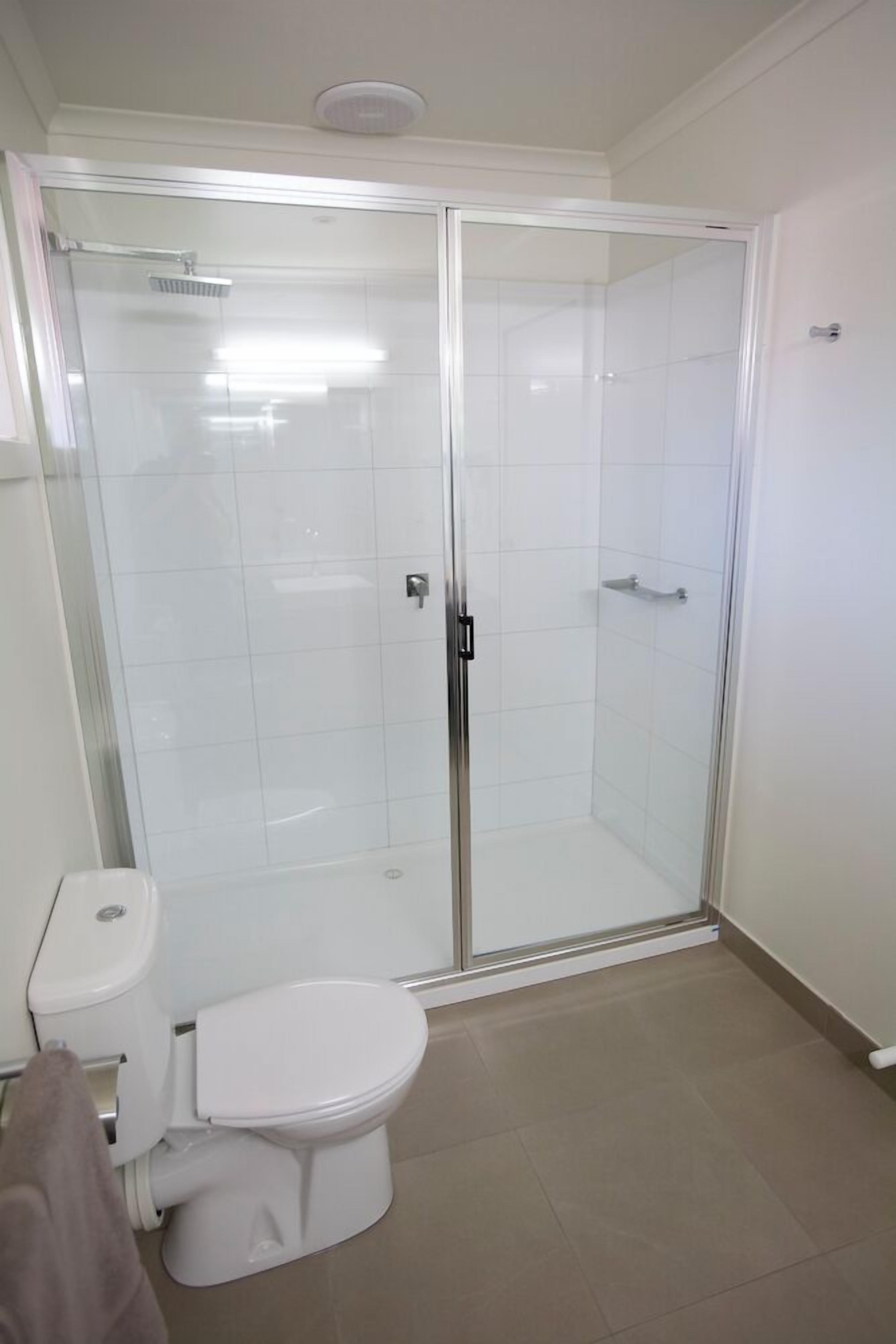Ein modernes Badezimmer mit einer gläsernen Duschkabine, einer weißen Toilette und einem beige gefliesten Boden.