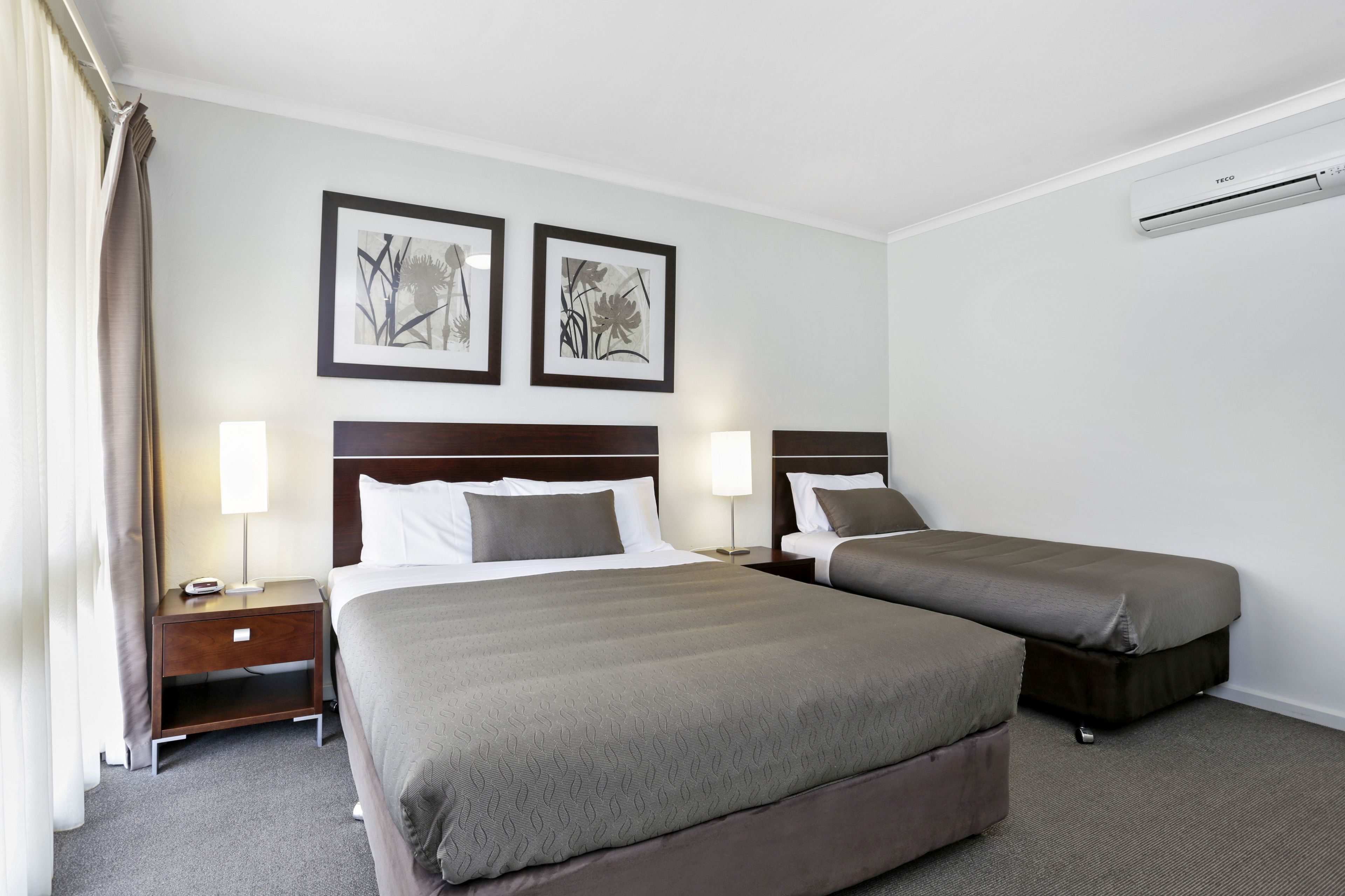 A hotel room with two beds, a nightstand with a lamp, and two framed pictures on the wall.