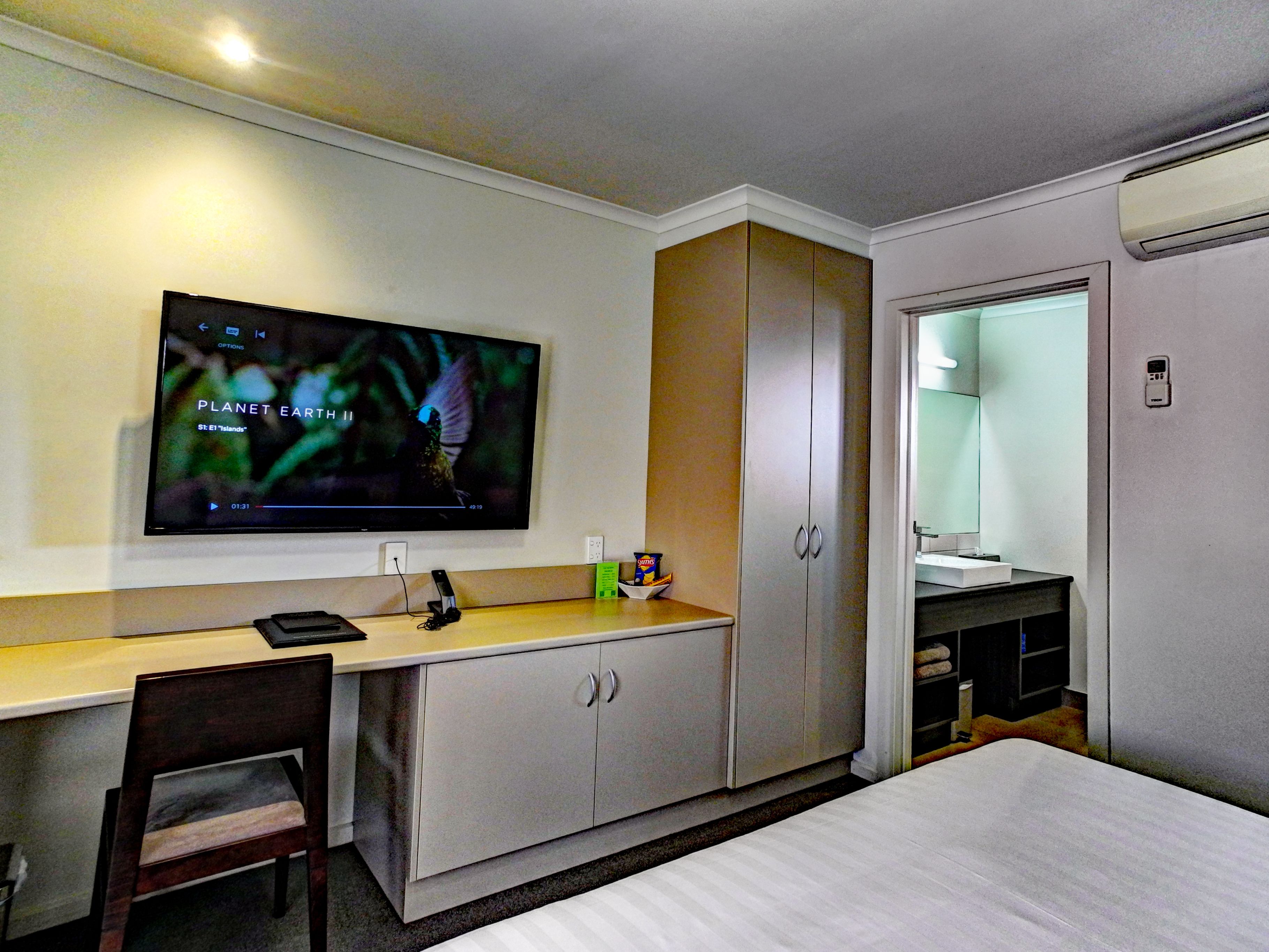 Une chambre d’hôtel comprenant un lit, un bureau avec une chaise, une télévision, une armoire et une salle de bain avec un miroir.
