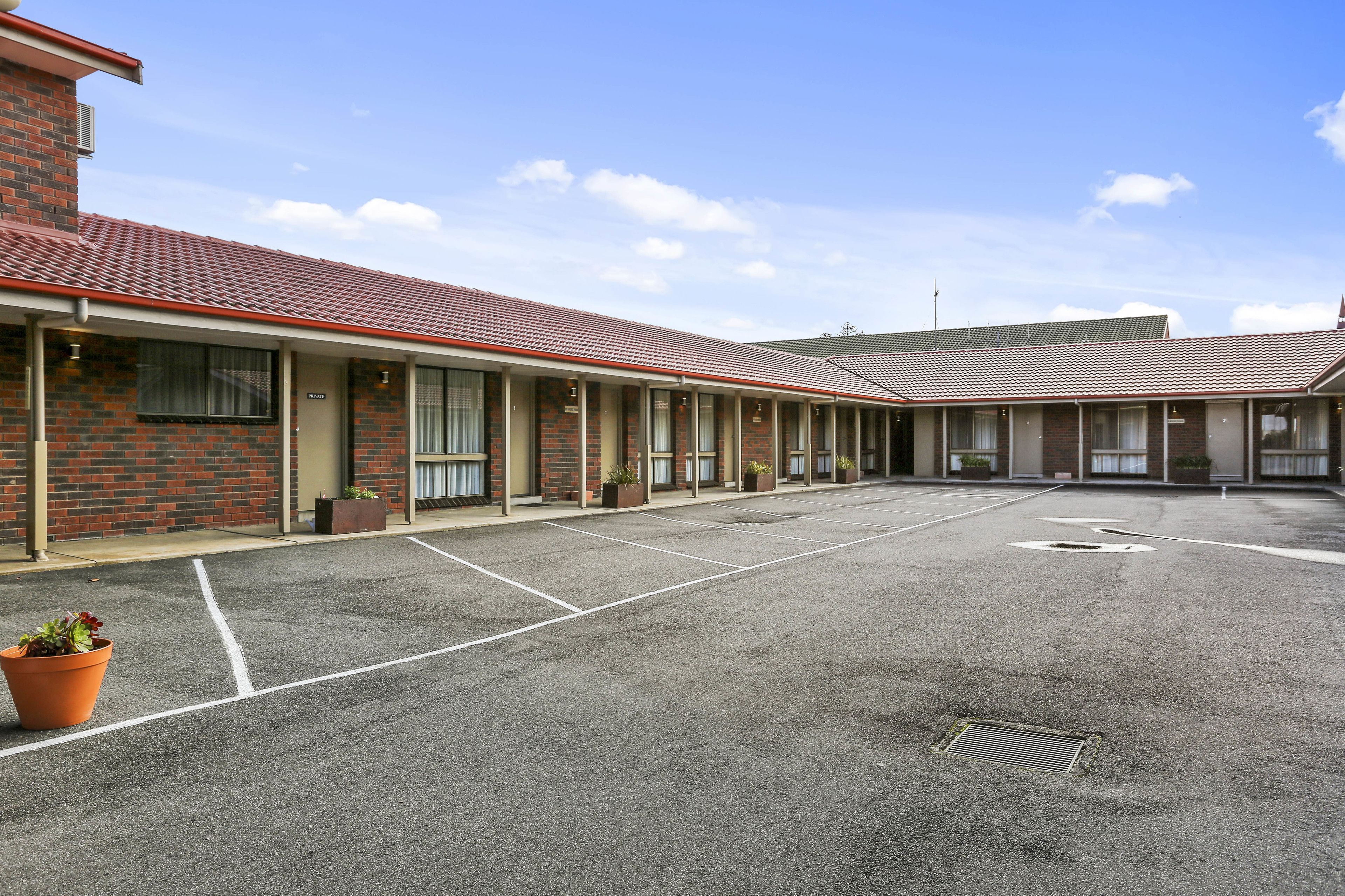 A motel with a row of rooms, a parking lot, and a brick building.