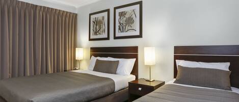 A hotel room with two beds, a wooden headboard, a nightstand with a lamp, and two framed pictures on the wall.