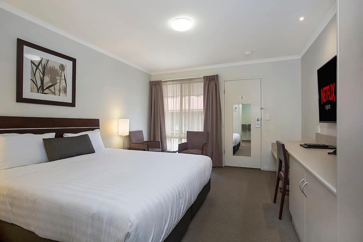 Una habitación de hotel con una cama grande, un escritorio con una silla, un televisor y una puerta que da a un baño.