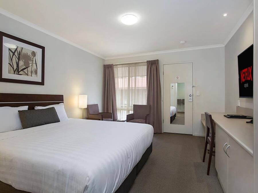 A hotel room with a large bed, a desk with a chair, a TV, and a door leading to a bathroom.
