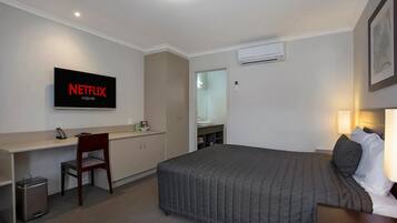 Habitación de hotel con cama, escritorio, silla y televisor que muestra 'NETFLIX originals', además de un equipo de aire acondicionado.