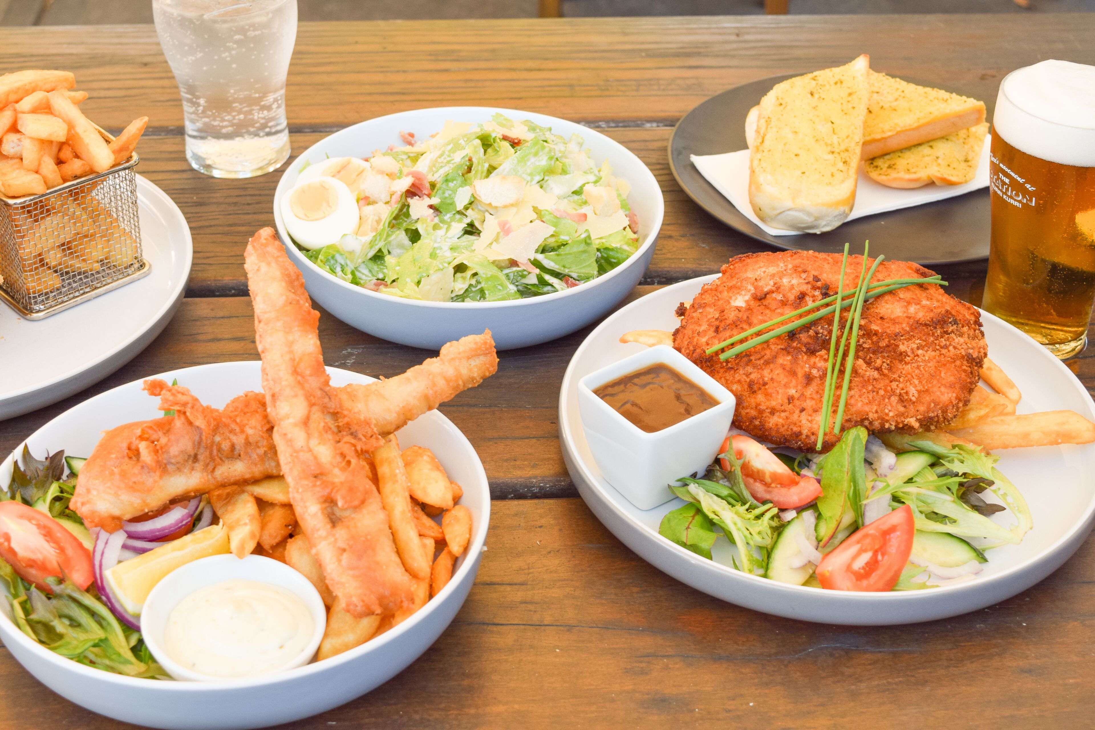 Una mesa con varios platos, incluyendo pescado con papas fritas, una ensalada y una cerveza.