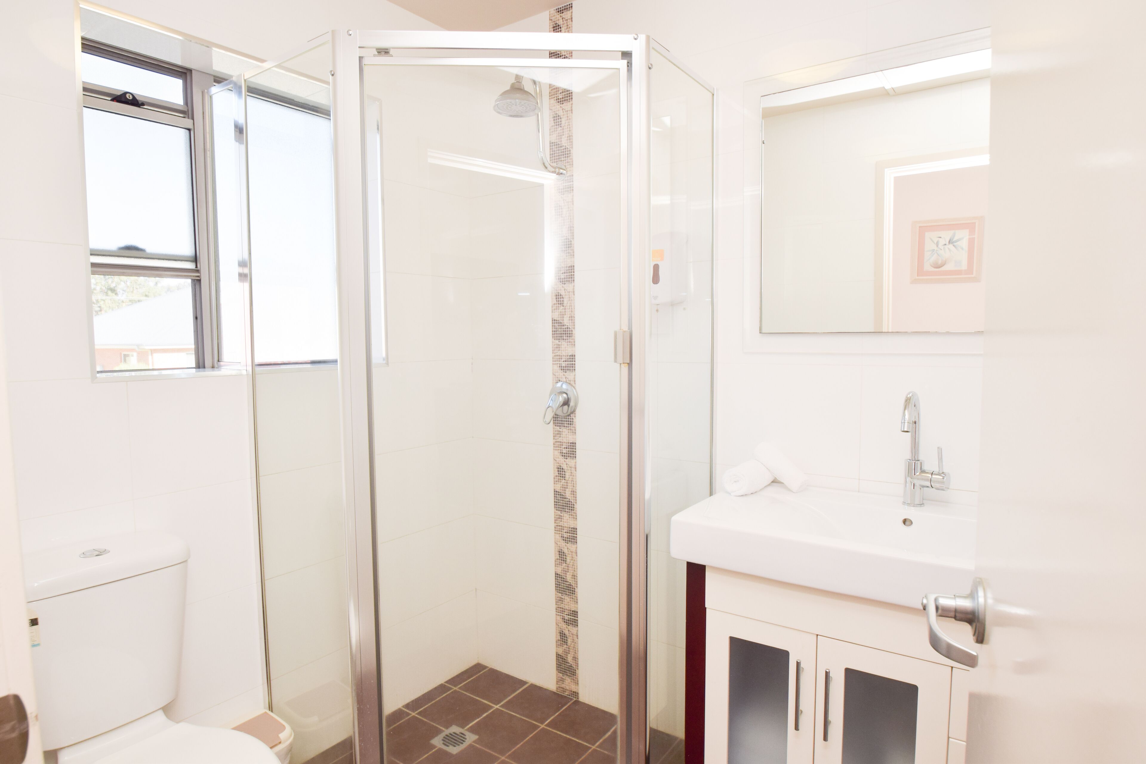 Een moderne badkamer met een douchecabine van glas, een toilet en een wastafel met spiegel erboven.