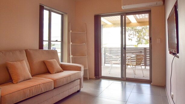 A living room with a sofa, a TV mounted on the wall, and a sliding glass door leading to an outdoor patio. - Station Hotel Motel Kurri Kurri (Kurri Kurri)