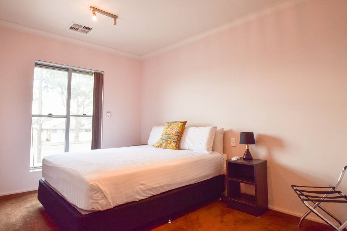A bedroom with a bed, bedside table, lamp, chair, window, and a door.