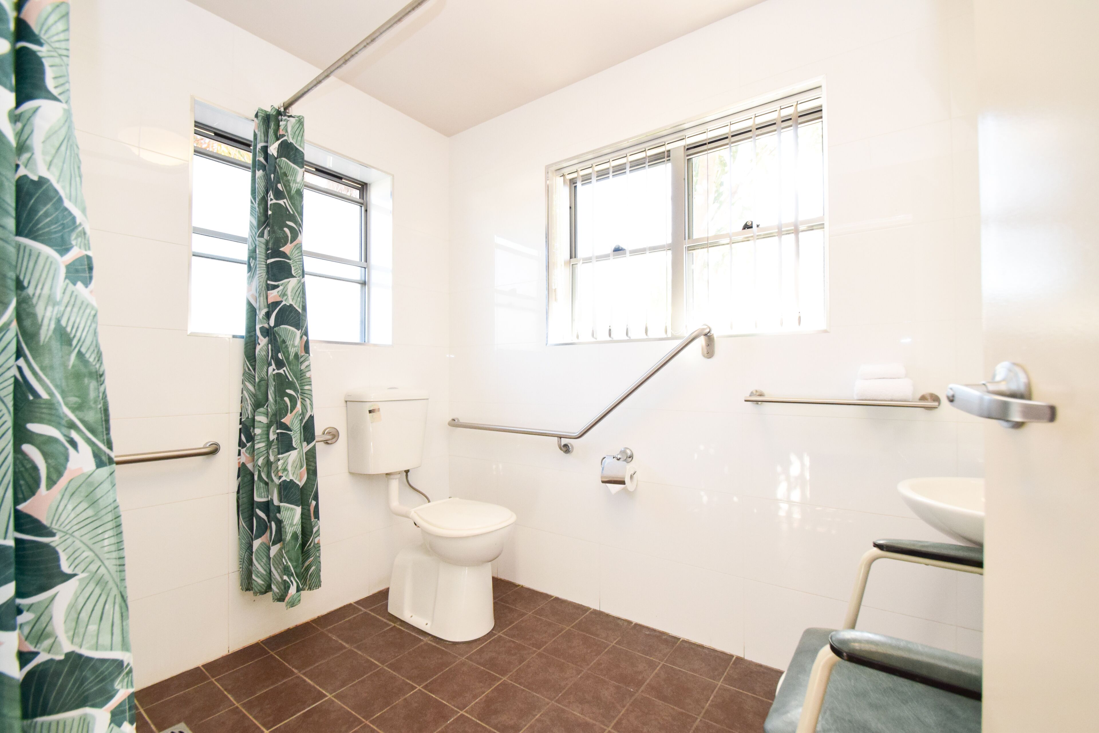 A bathroom with a toilet, a shower with a curtain, a window, and a sink.