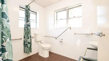 A bathroom with a toilet, a shower with a curtain, a window, and a sink.