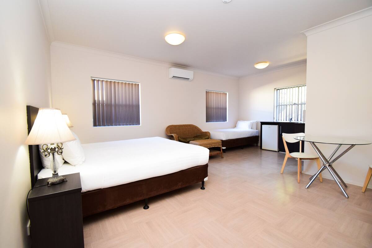 A hotel room with a large bed, a desk, two chairs, and a lamp.
