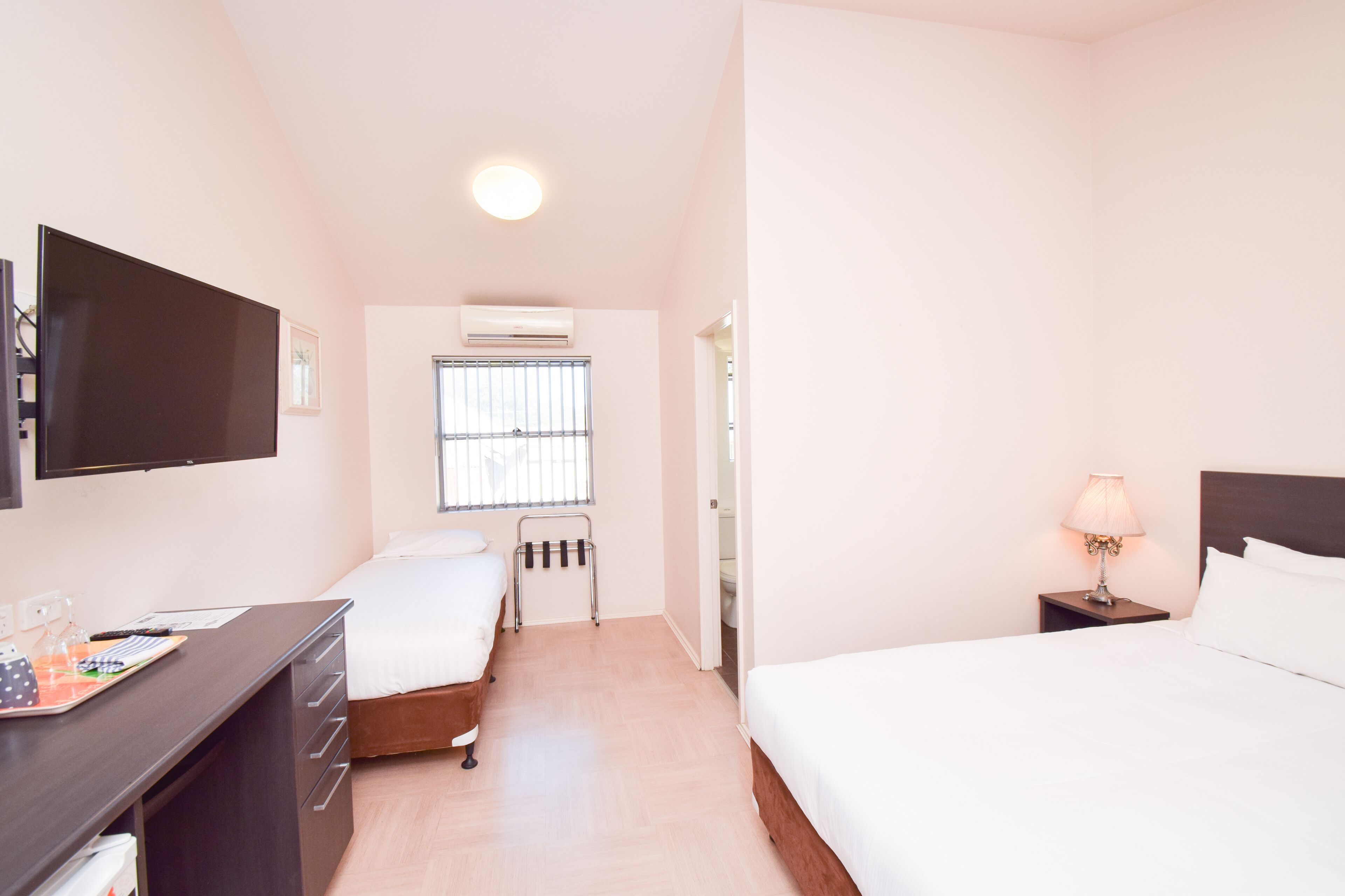 A hotel room with a bed, a desk, a TV, a window, and a bedside lamp.