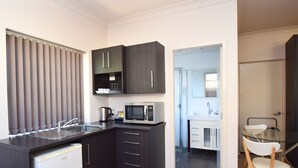 A compact kitchen with dark cabinetry, a microwave, a sink, and a small refrigerator. - Station Hotel Motel Kurri Kurri (Kurri Kurri)
