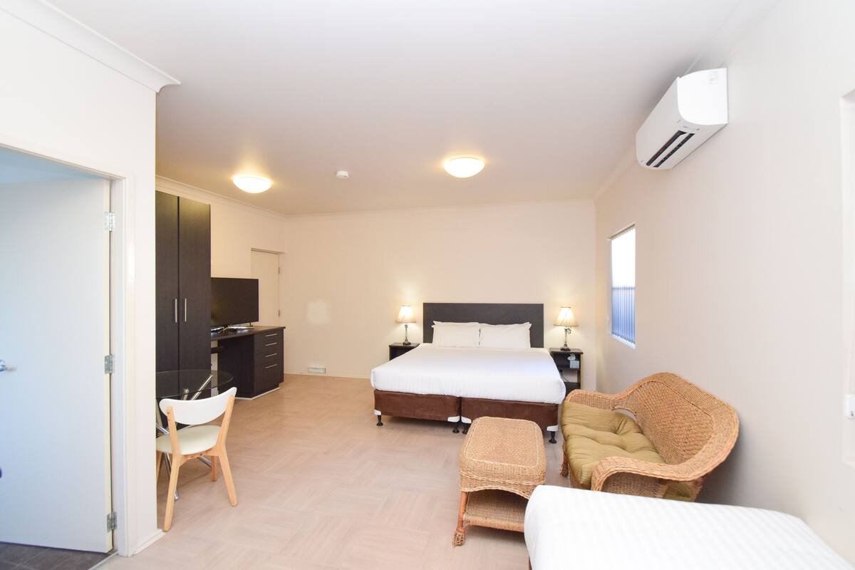 A bedroom with a bed, bedside tables, a chair, a small table, and an air conditioning unit.