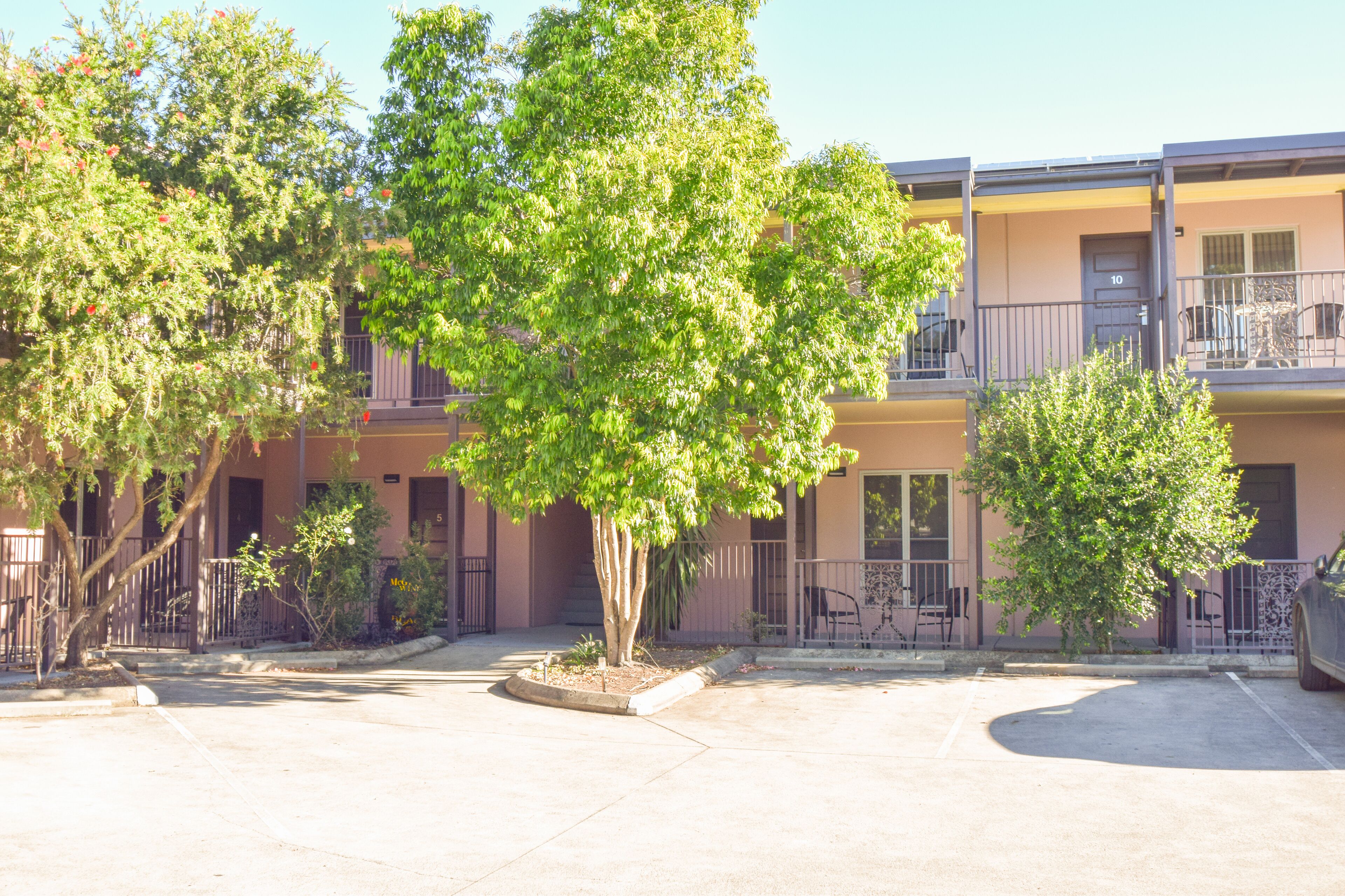 A multi-story building with balconies, a parking lot, and trees.