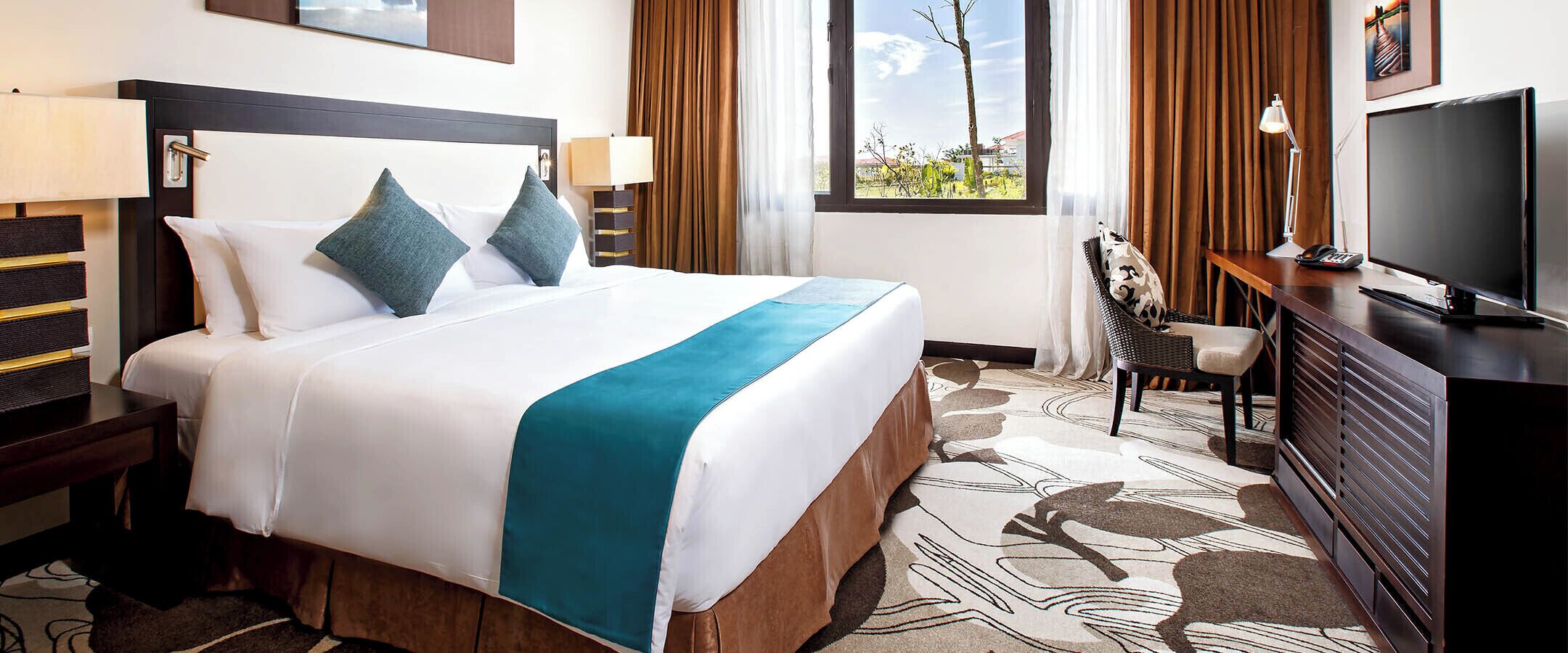 A hotel room with a bed, a desk, a TV, and a window with a view.