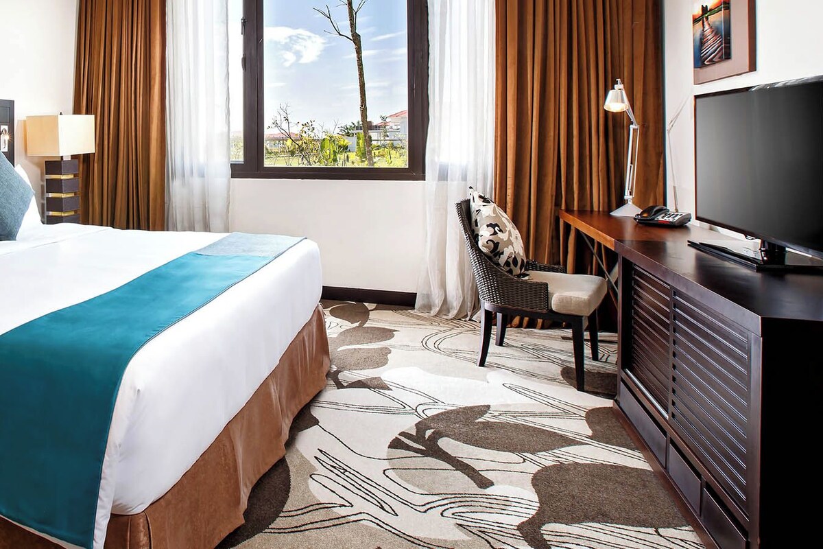 A hotel room with a bed, a desk, a TV, and a window with a view.