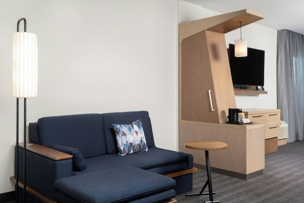 Una habitación de hotel moderna con sofá, una mesita, televisión y kitchenette.