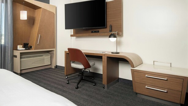 A hotel room with a bed, a desk with a chair, a television, a desk lamp, and a small drawer unit. - Courtyard by Marriott Houston NW/290 Corridor (Houston)