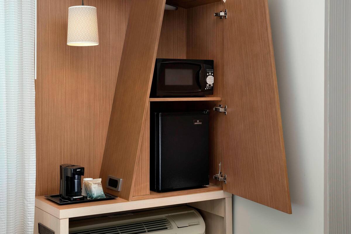 Una kitchenette compacta con microondas, un refrigerador pequeño y una cafetera.
