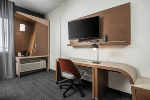 A hotel room with a wooden desk, a flat-screen TV mounted on the wall, a chair, a desk lamp, and a heater under the desk. - Courtyard by Marriott Houston NW/290 Corridor (Houston)