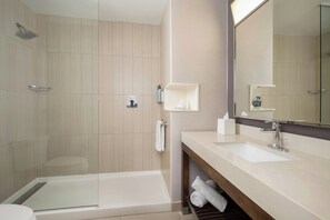 A modern bathroom with a glass-enclosed shower, a bathtub, a vanity with a sink, and a large mirror. - Courtyard by Marriott Houston NW/290 Corridor (Houston)