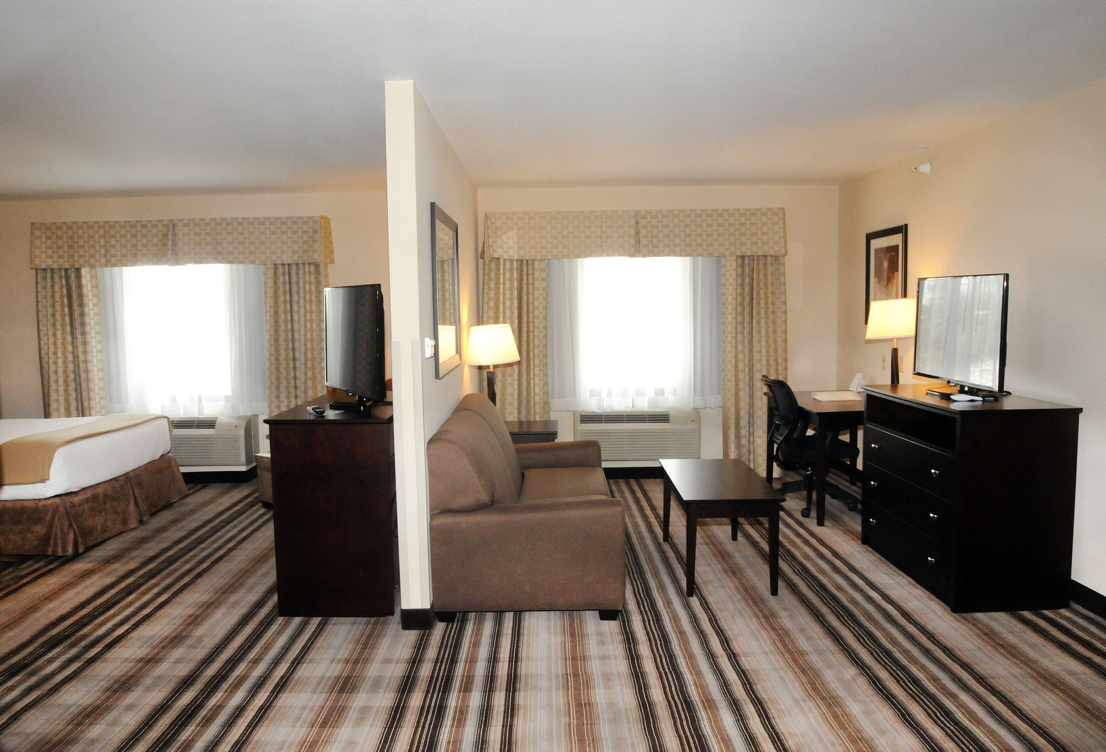 A hotel room with a bed, a sofa, a desk, a television, and a dresser.