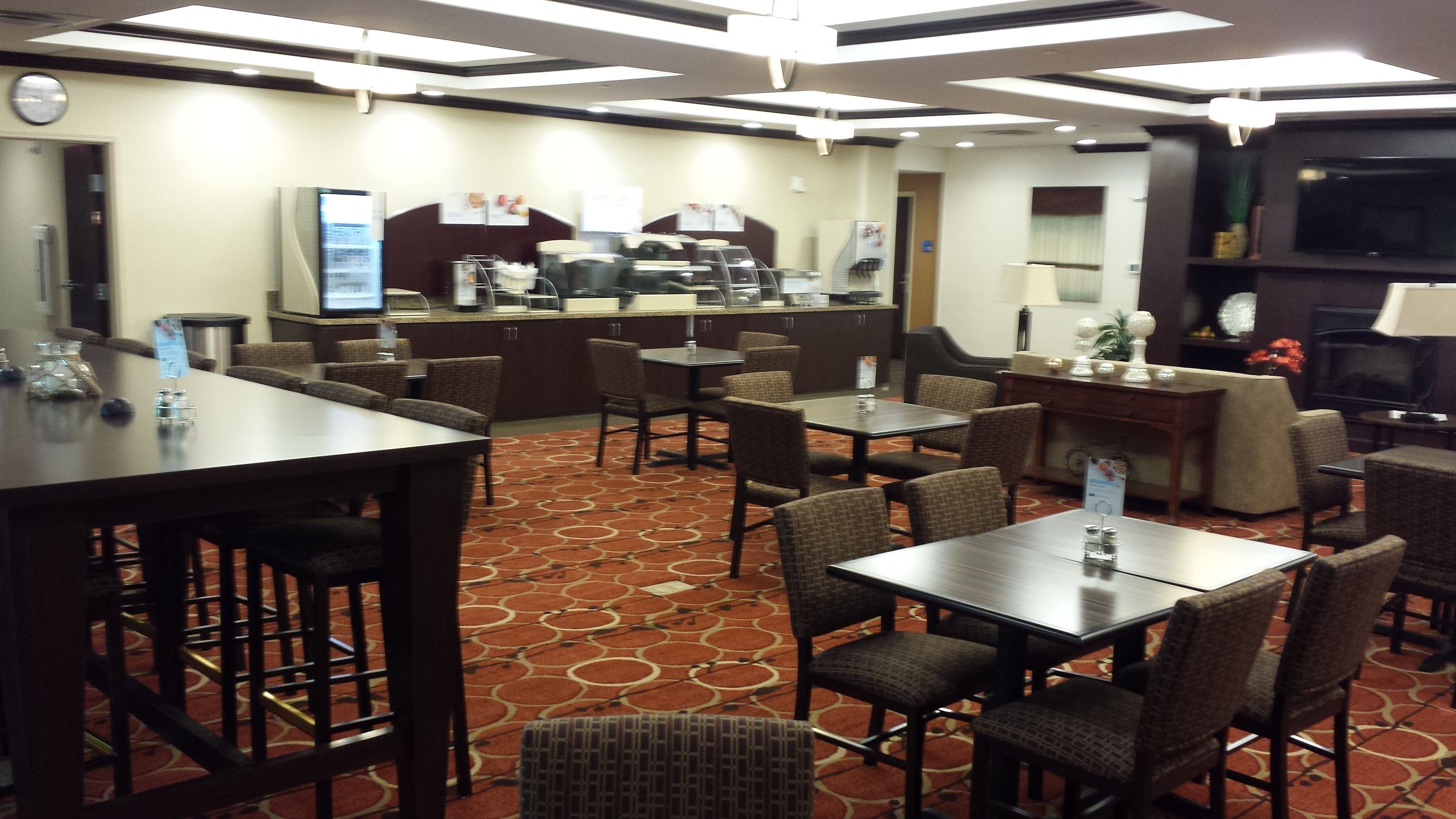 Un comedor de hotel con mesas y sillas redondas, una barra de buffet y un televisor al fondo.