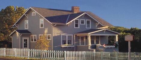 A two-story house with a white picket fence, a front porch, and a chimney.