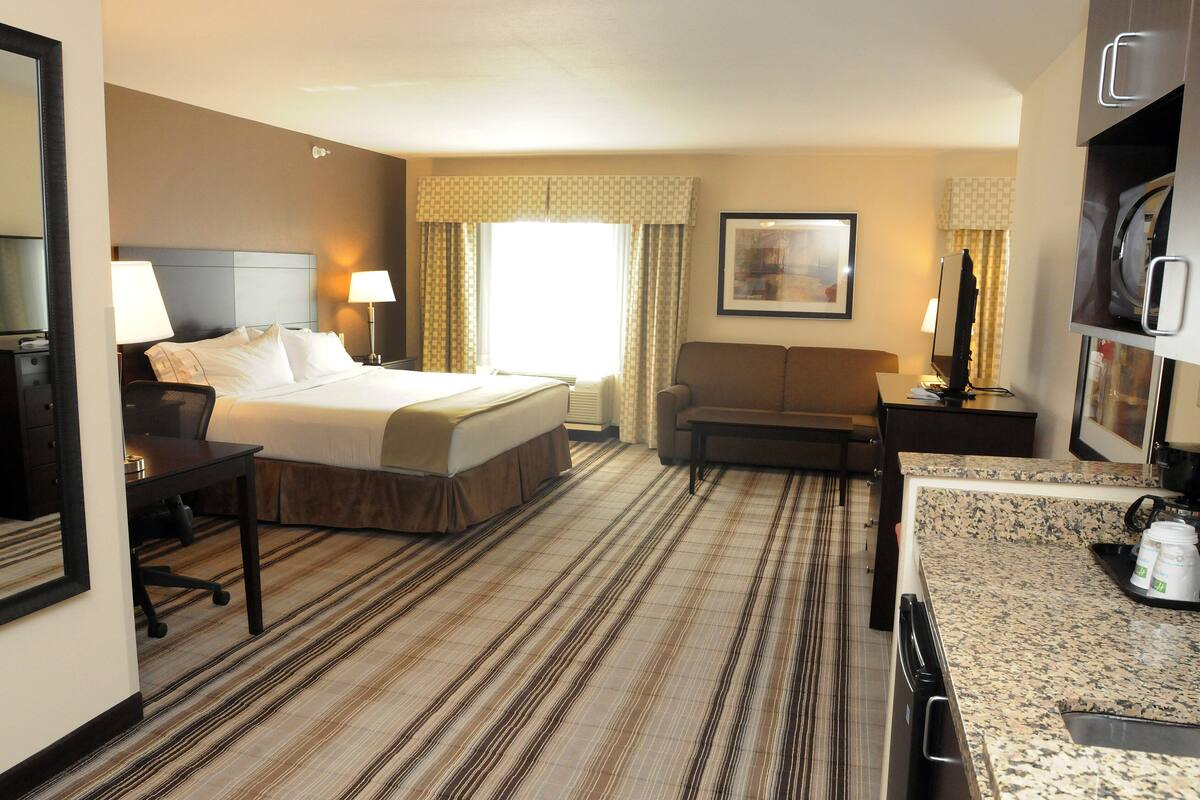 A hotel room with a bed, desk, chair, and a kitchenette area.
