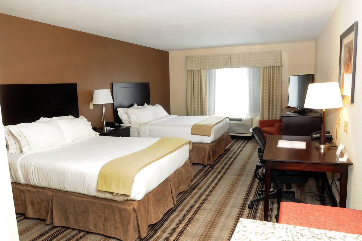 A hotel room with two beds, a desk, a chair, a TV, and a window with curtains.