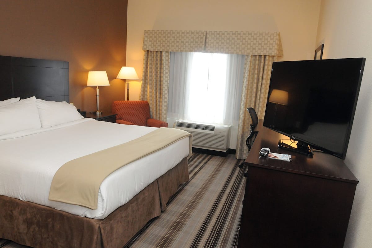 A hotel room with a large bed, two bedside lamps, a flat-screen TV, a desk with a telephone, and a window with curtains.
