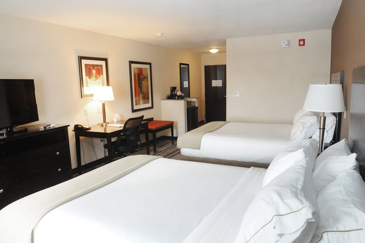 A hotel room with two beds, a desk with a chair, a television, and a coffee machine.
