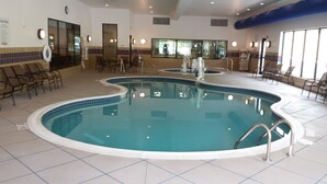 Ein Hallenbad mit mehreren Bahnen, Liegestühlen und einem Poolbereich mit Blick ins Freie.
