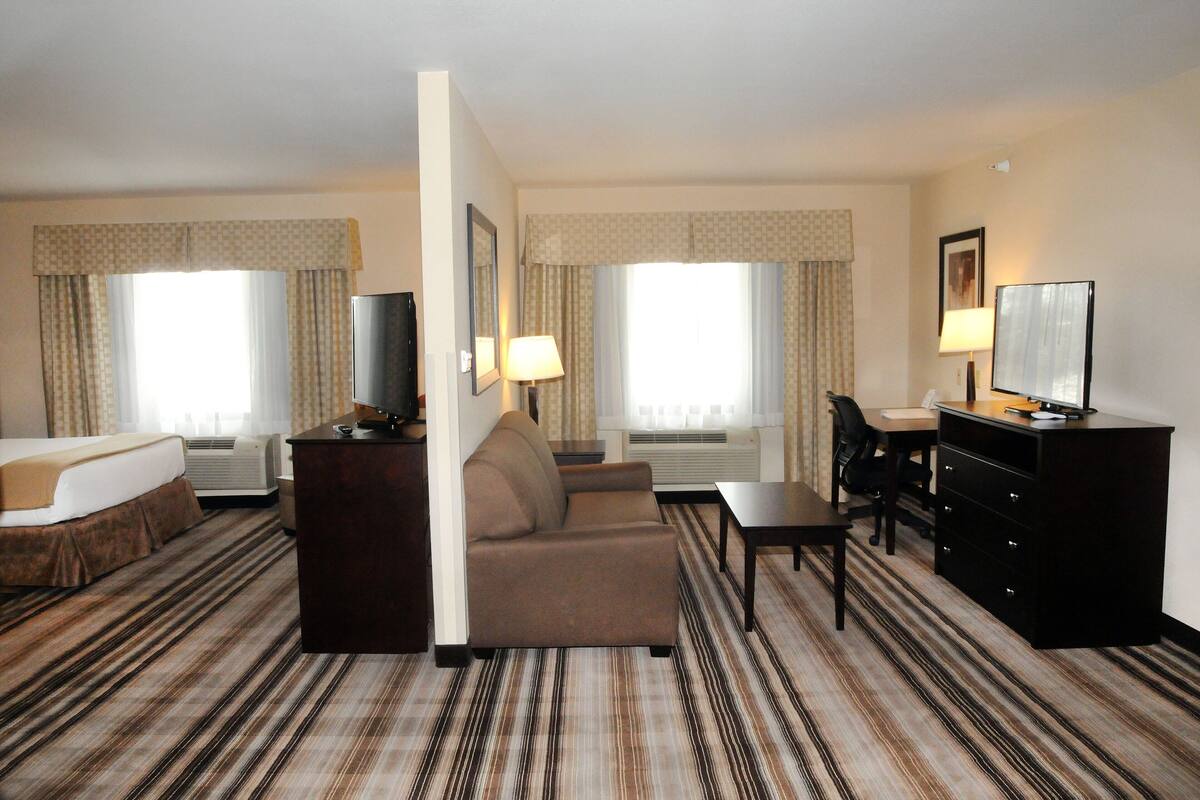 A hotel room with a bed, a sofa, a desk, a TV, and a dresser.