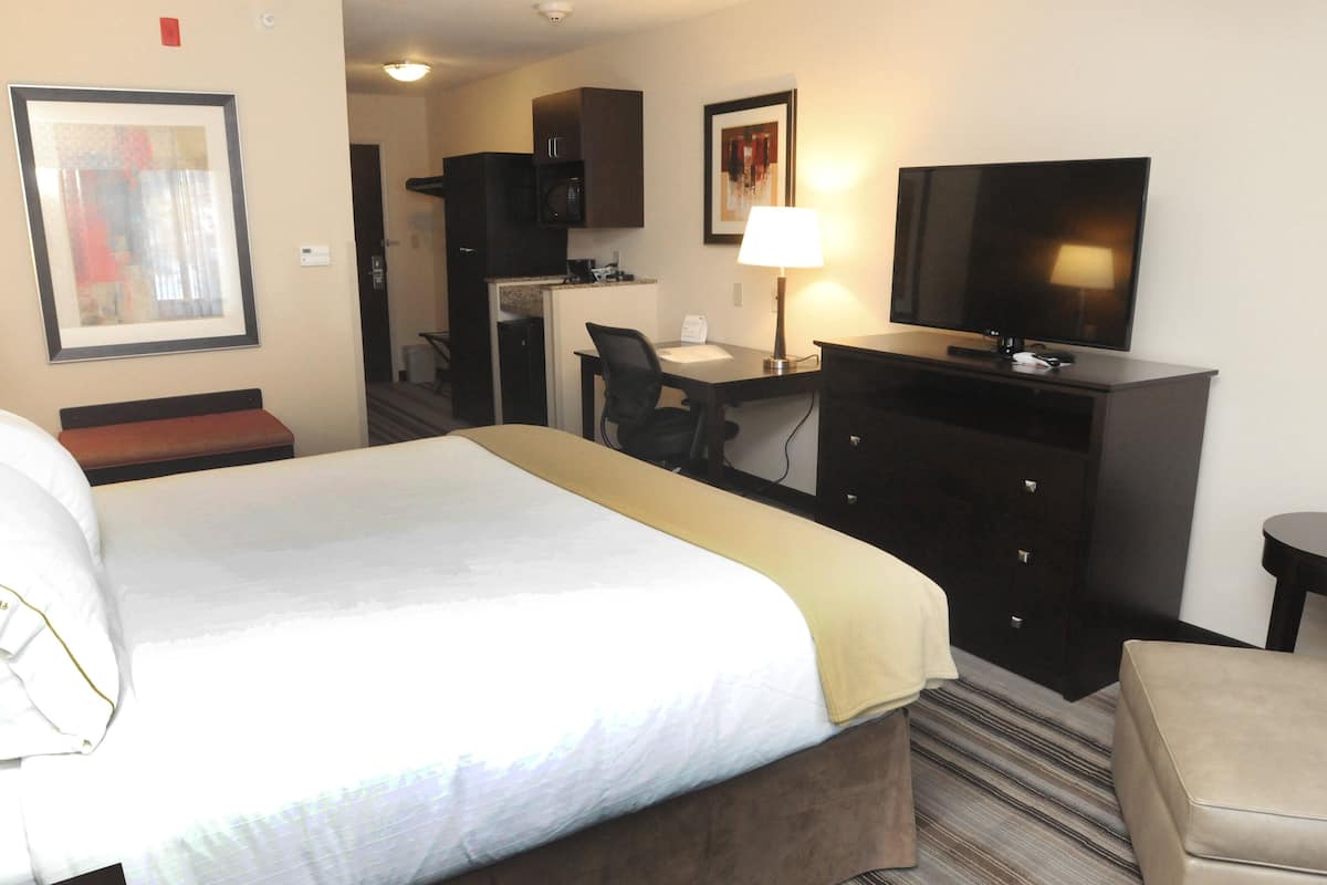 A hotel room with a bed, a desk with a chair, a television, a small kitchenette, and a bathroom.