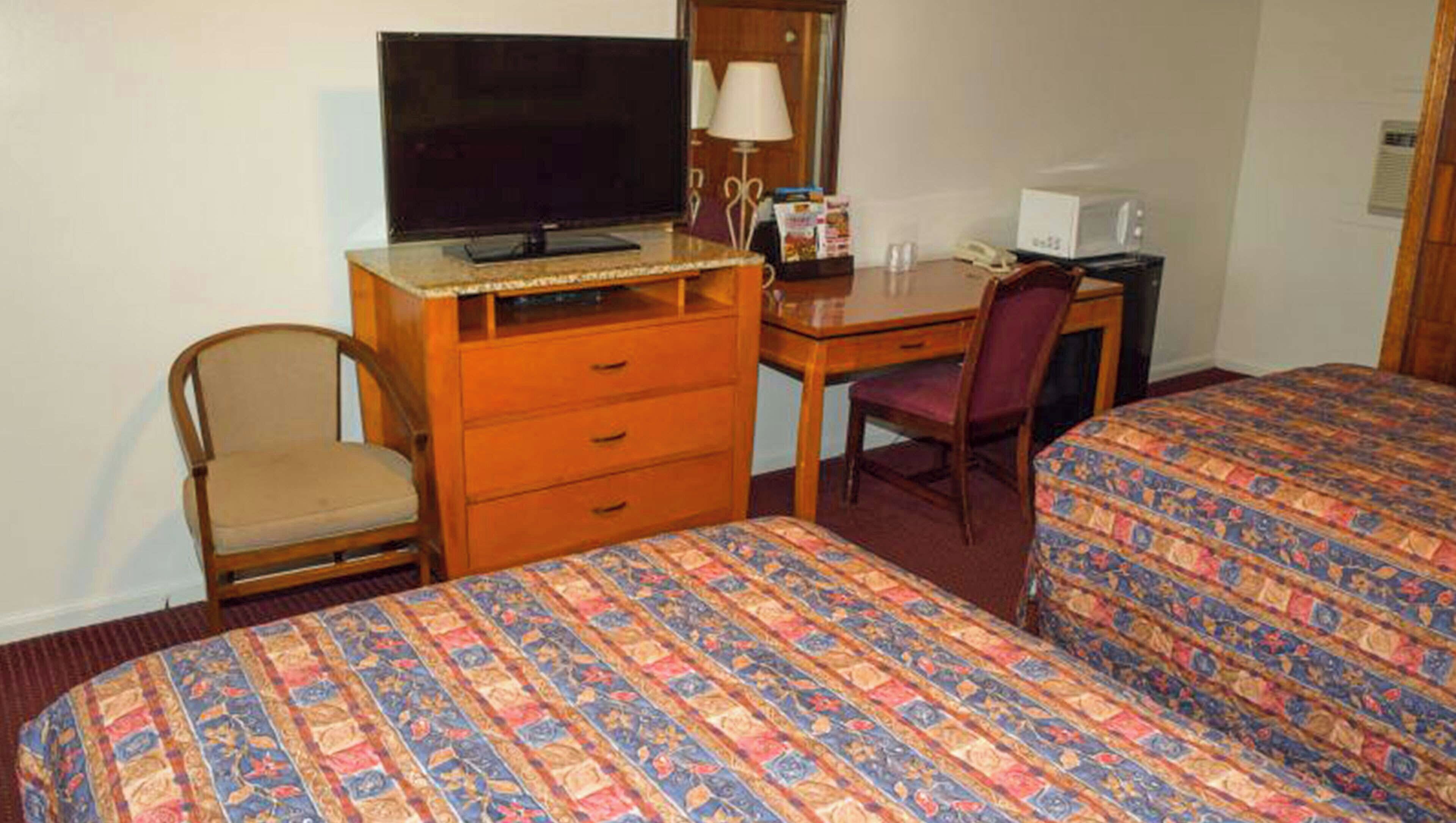 Een hotelkamer met twee bedden, een bureau met televisie, een stoel, een kast en een magnetron.