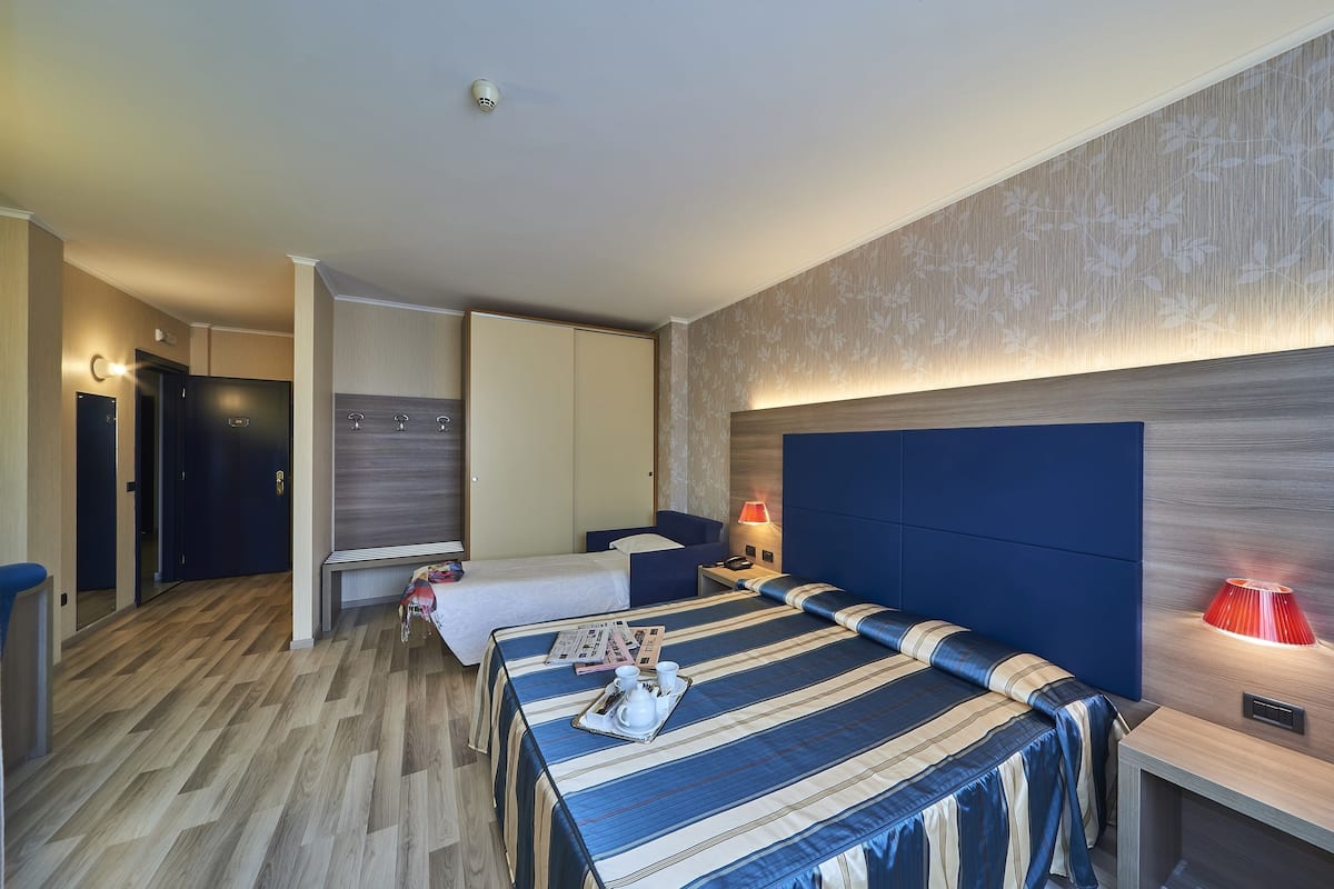 A hotel room with two beds, a desk, a lamp, and a bathroom door.
