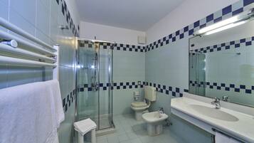 Un baño con cabina de ducha de vidrio, inodoro, bidé y lavabo con espejo.
