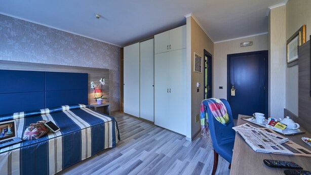 A hotel room with a sofa, a desk with a laptop, a chair, a wardrobe, and a door. - Hotel Alberi (Lecco)