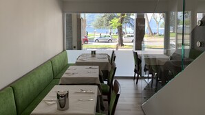 Restaurante con un área de asientos con bancos acolchados verdes, mesas con cubiertos y vistas a una calle con coches y árboles.