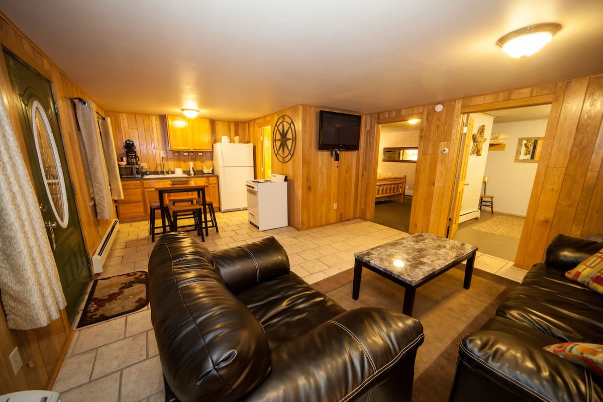 A cozy living room with a leather sofa, a coffee table, and a TV mounted on the wall.